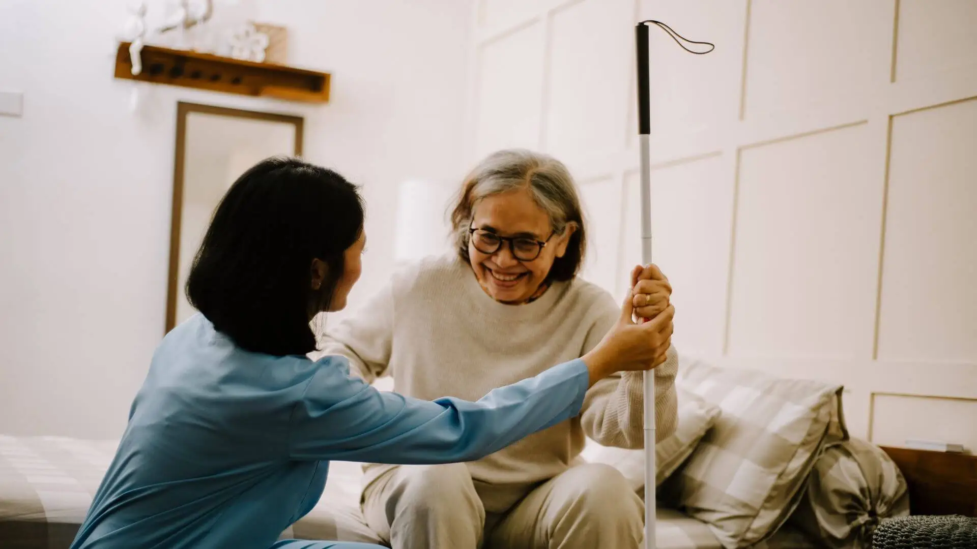 护理员帮助老人起身，两人开心微笑 — a caregiver helping an elderly parent with warmth and care